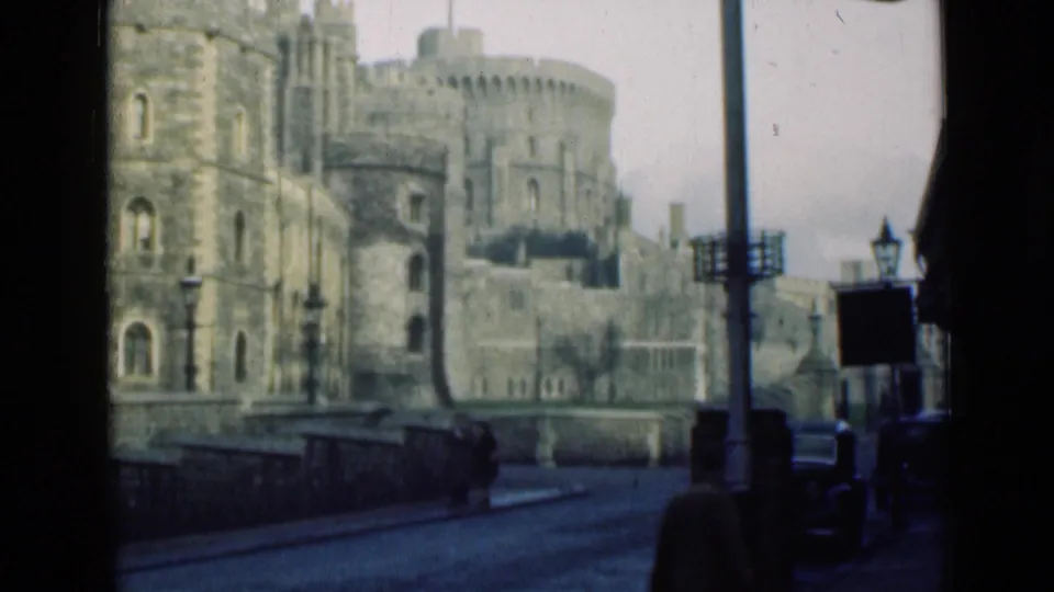 Windsor Castle remains in view as a street pole, sign, pedestrians, and a dark vehicle appear in the 1946 home-movie frame.