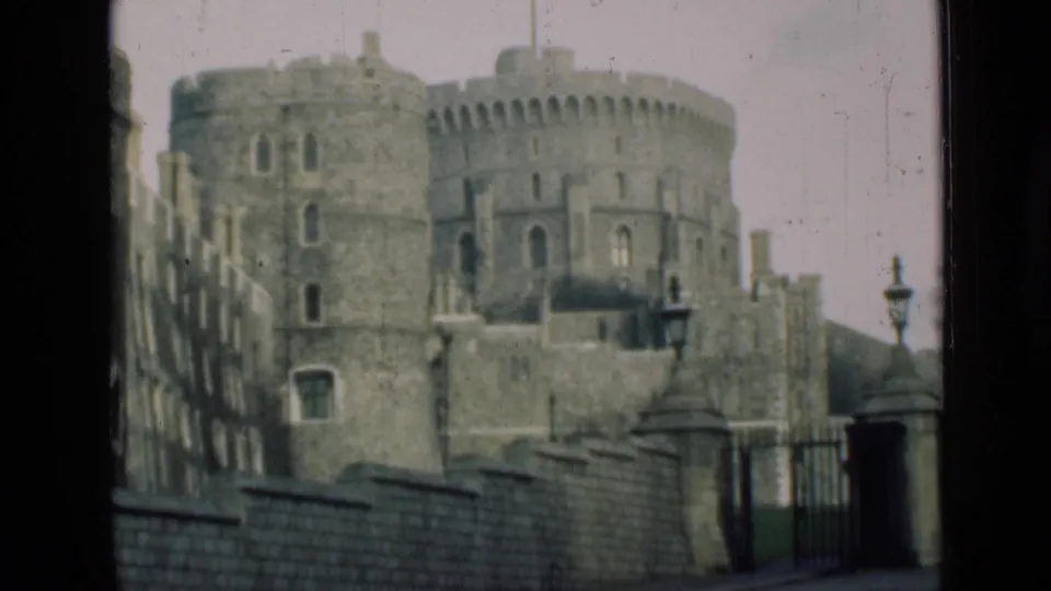 Windsor Castle towers and battlements fill the frame behind iron railings, a low wall, and street lamps in faded 8mm color.