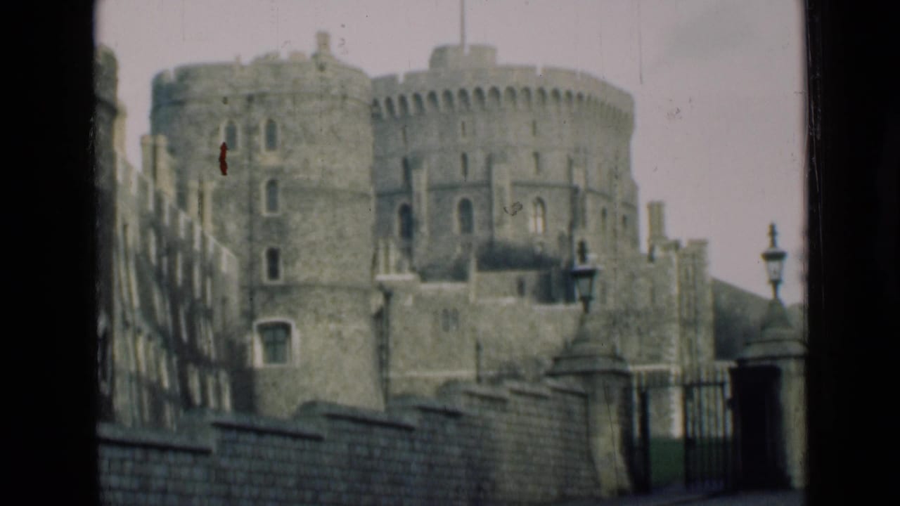 1946 8mm view of Windsor Castle showing round stone towers, battlements, a wall, gate area, and lampposts from a distant visitor perspective.