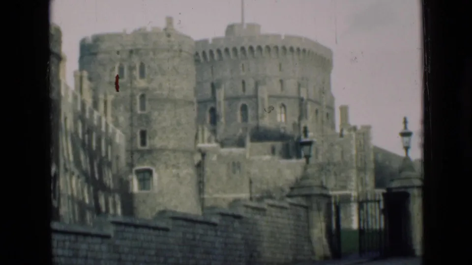 1946 8mm view of Windsor Castle showing round stone towers, battlements, a wall, gate area, and lampposts from a distant visitor perspective.