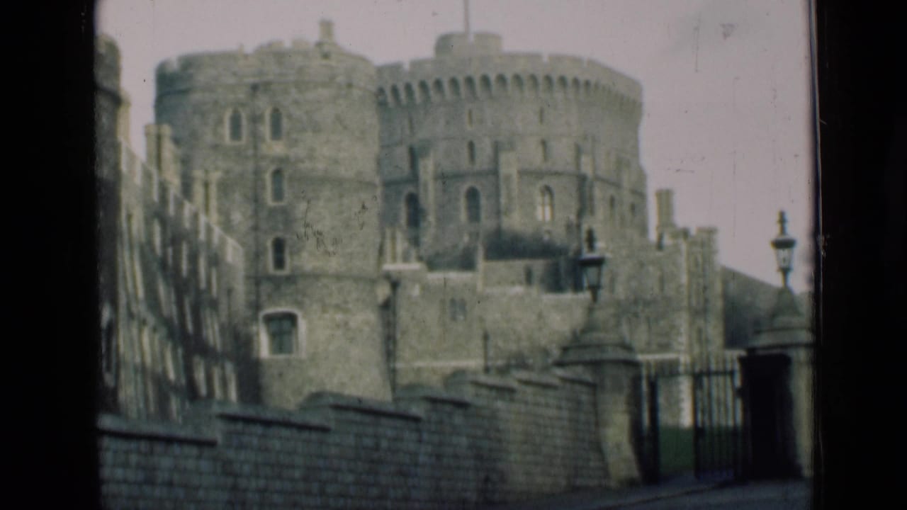Castle towers, battlements, stone wall, gate, and lampposts seen through dark framing.