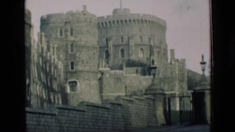 Windsor Castle appears in soft 8mm color with round towers, battlements, a stone wall, iron gate, and lampposts visible through a dark frame edge.