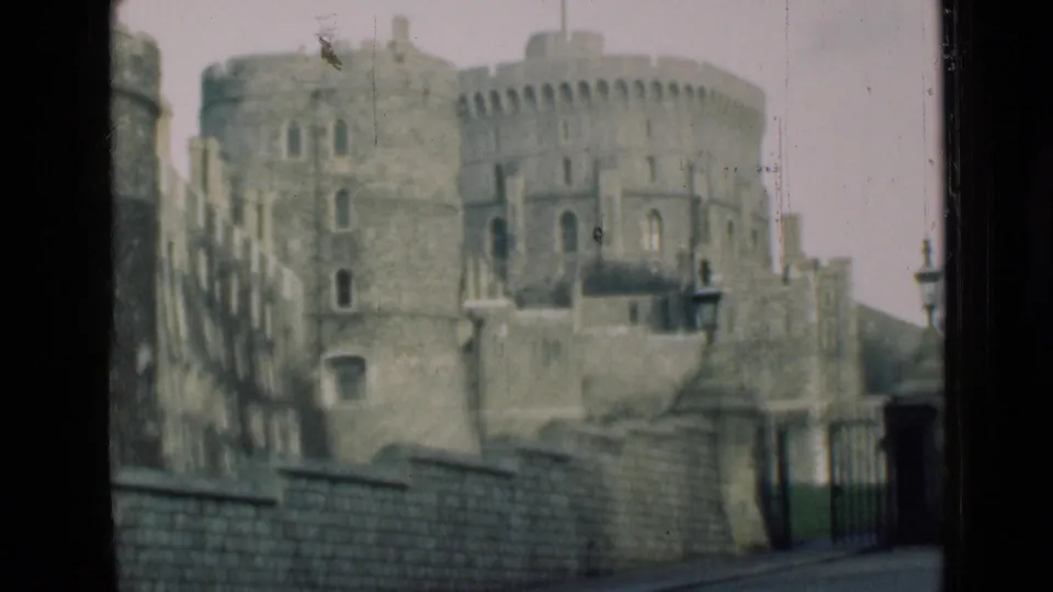 Final frame holds on Windsor Castle's round towers, battlements, foreground wall, gate, and lampposts, with dark vertical borders suggesting a window or film edge.