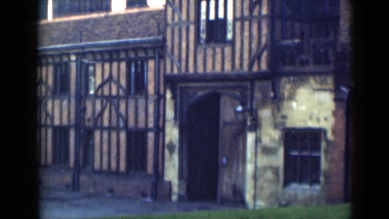 Timber-framed building facade with arched wooden door, iron fence and stone wall section.