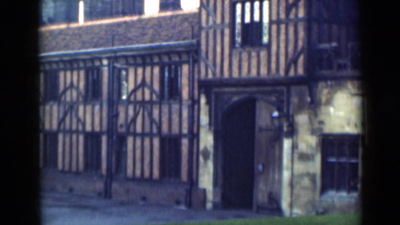 Timber-framed facade with dark beams, arched doorway, iron fence and upper windows.