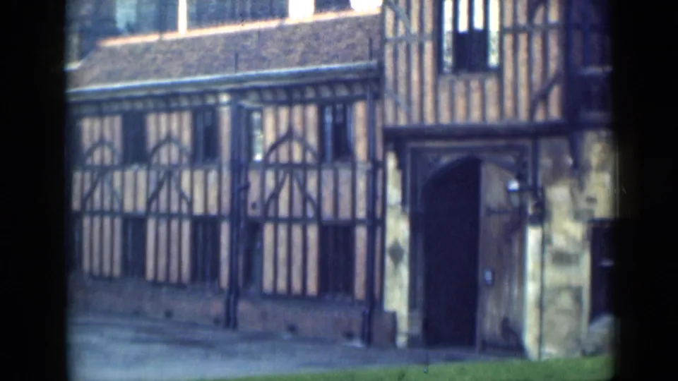 1946 London home-movie frame showing the timber-framed frontage with a large arched wooden door and fence in soft 8mm focus.