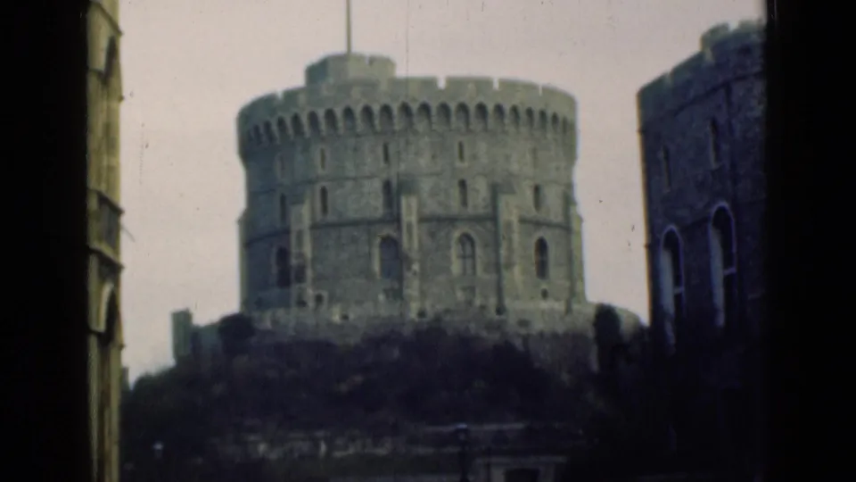 Soft 8mm 1940s view of Windsor Castle's Round Tower, centered between dark foreground framing and adjacent stone buildings.