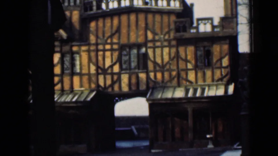 1946 8mm view of a Tudor-style timbered facade with small windows, roof trim, and an arched passage below.