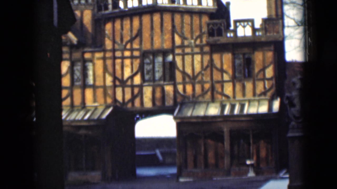 1946 London home-movie frame showing an orange timber-framed building, dark beams, small windows, and a central arch.