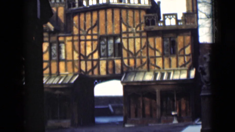 1946 London home-movie frame showing an orange timber-framed building, dark beams, small windows, and a central arch.
