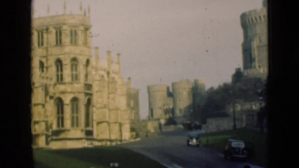 1946 England home-movie view of a stone castle approach, with towers, battlements, roadway, lawn, and classic cars.