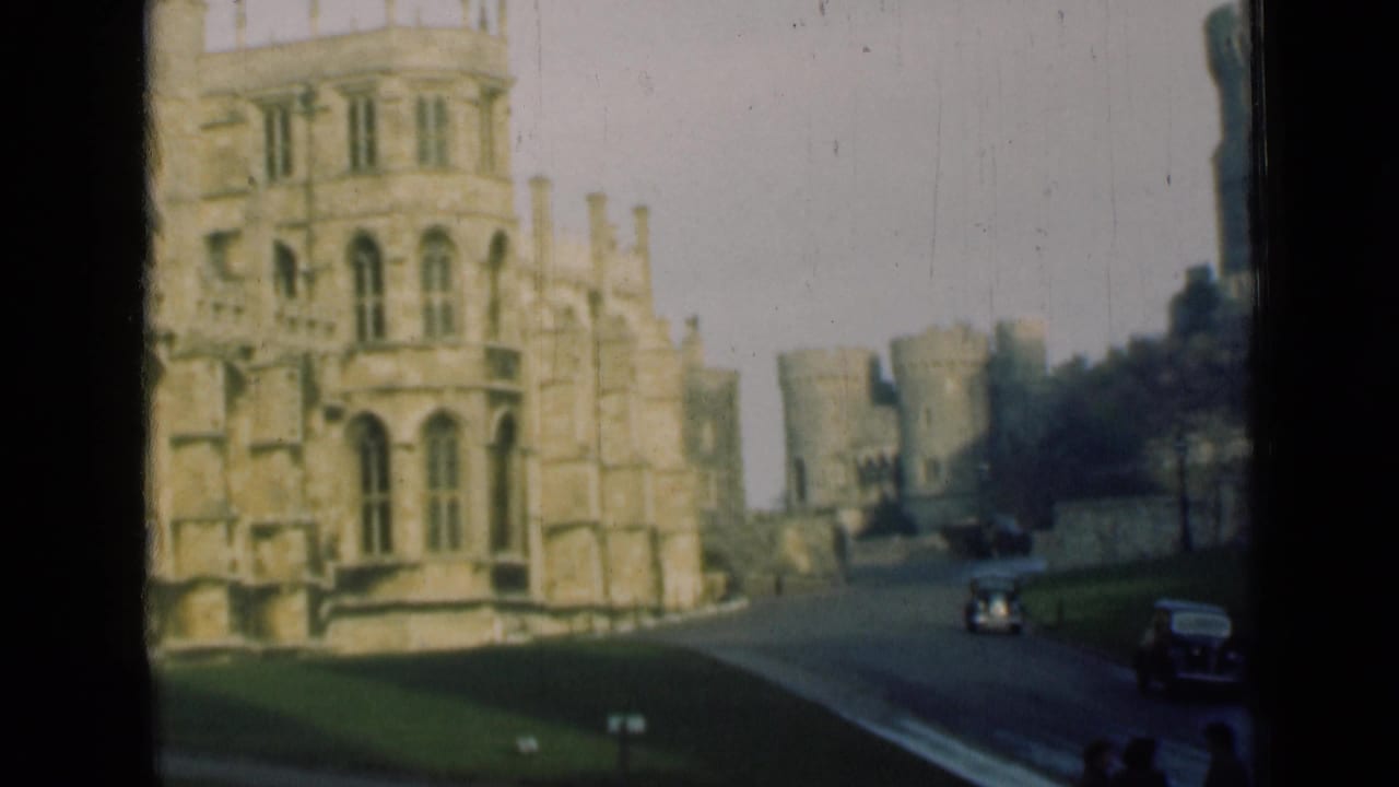 Castle buildings and turreted walls with cars on the road at right.