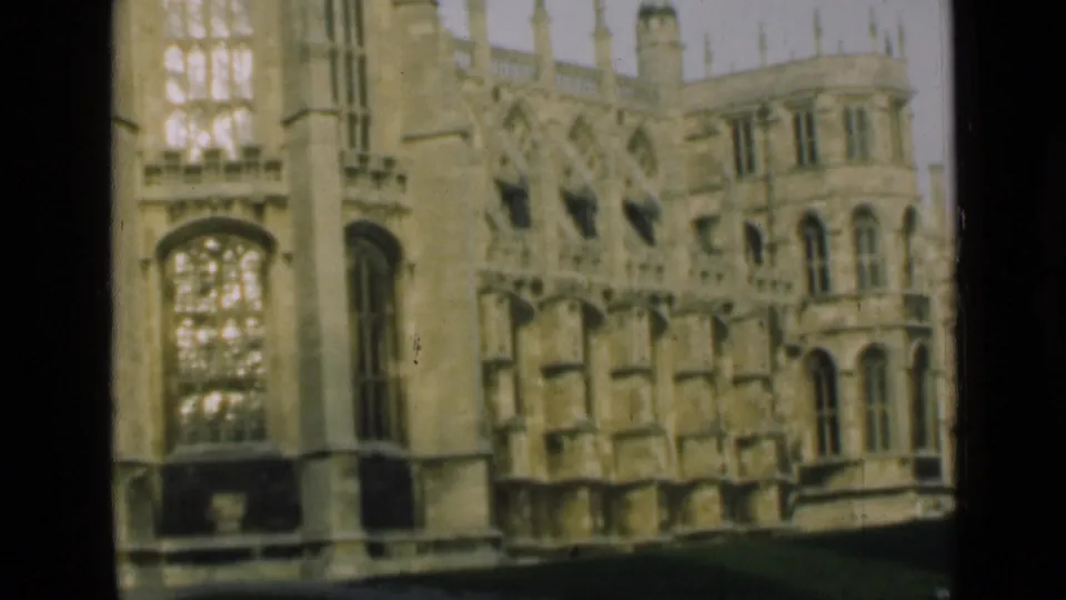 1946 London-area home-movie frame with a tall tracery window, adjacent stone wall, buttresses, and lawn below.
