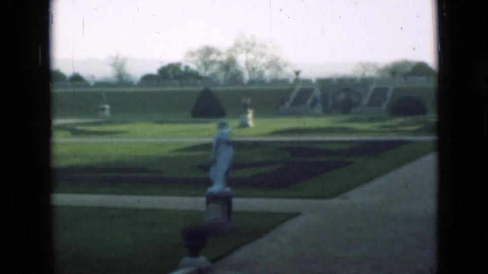 1946 London home-movie view across a formal garden with manicured lawns, geometric beds, paths and a statue.