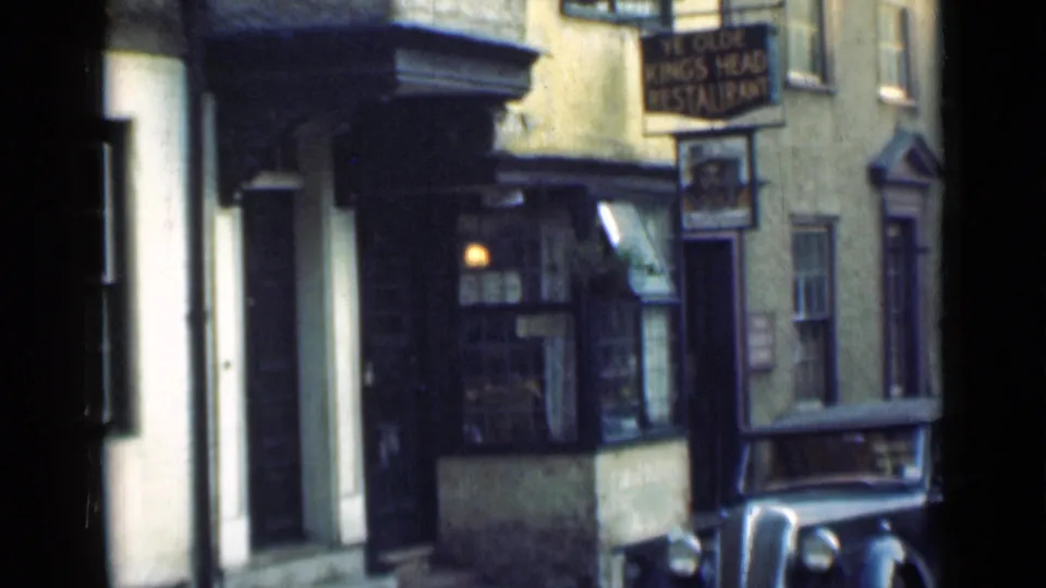 London pub exterior from 1946, with Ye Olde King's Head sign, window display area, pale facade, and vintage car in front.