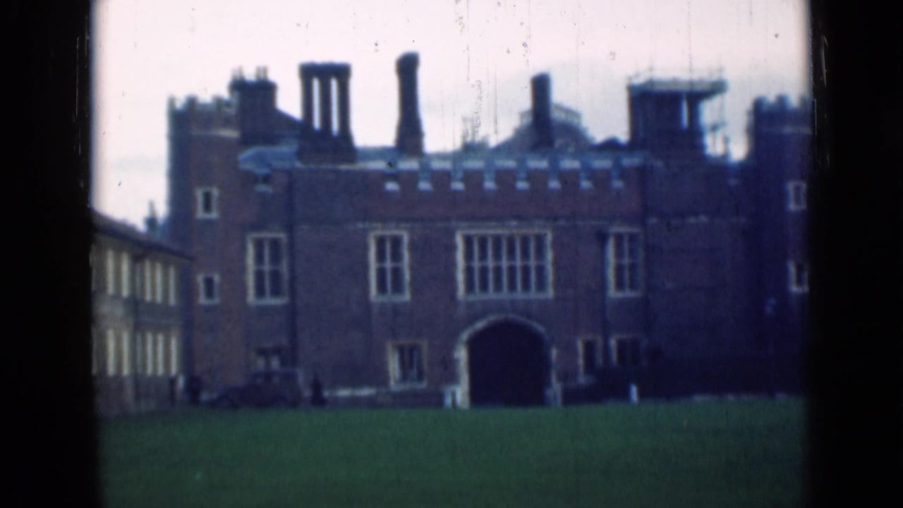 Large brick Tudor-style building with chimneys, lawn, windows, and an arched entrance.