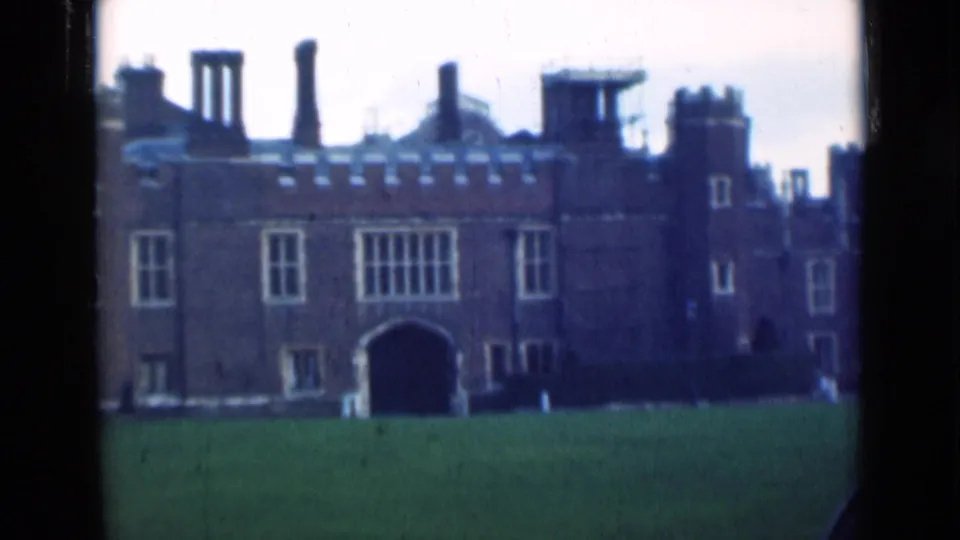 1940s London frame with a soft-focus view of a Tudor-style brick exterior, broad lawn, tall chimneys, windows, and central archway.