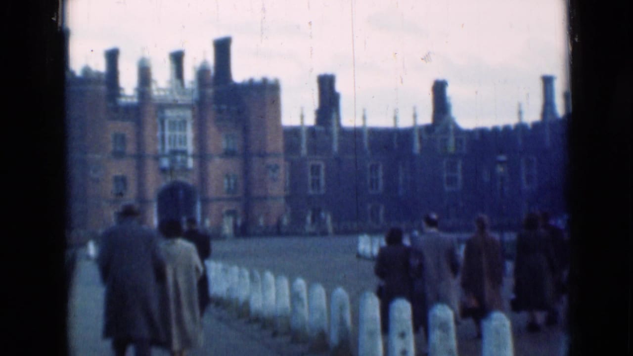 Visitors walk along a stone path toward a large brick Tudor-style palace.