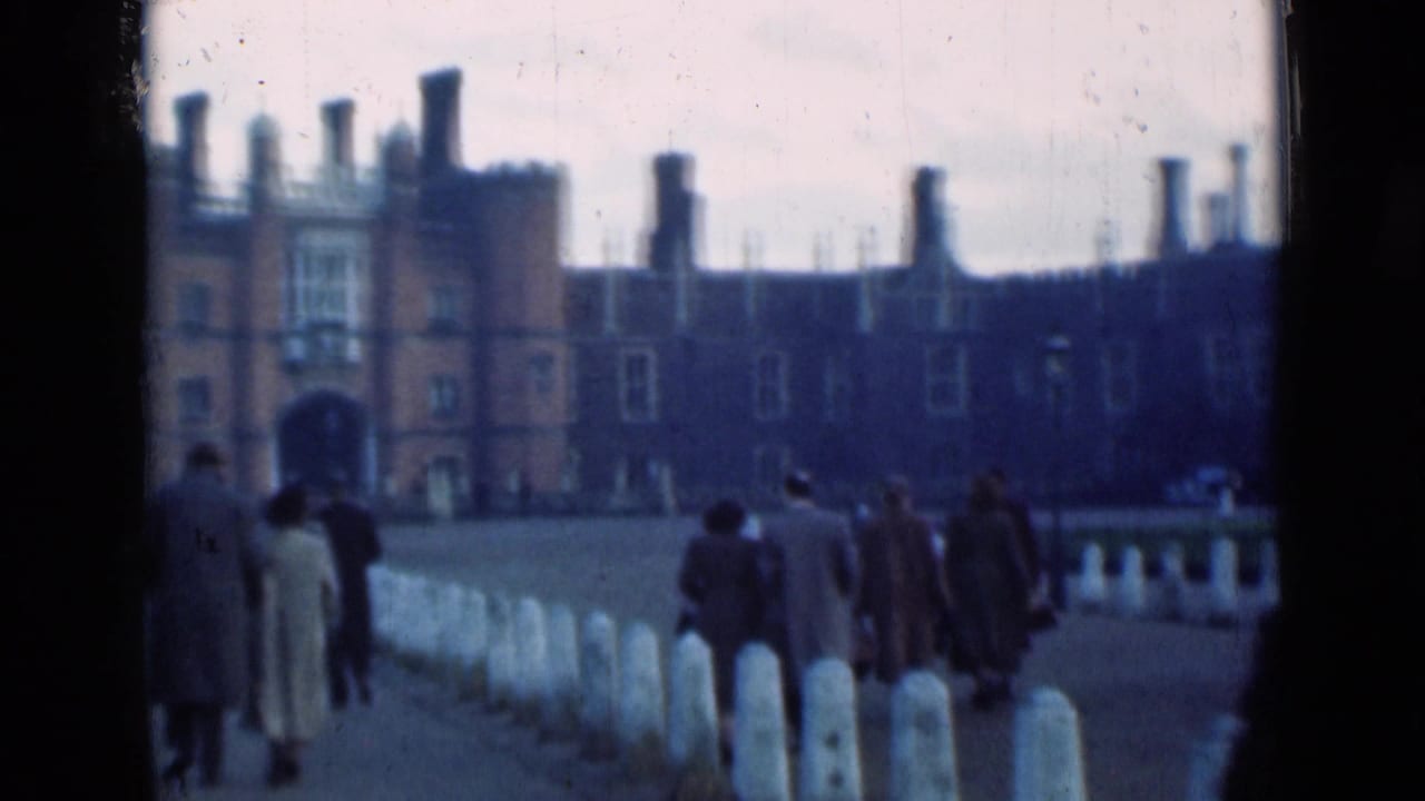 Visitors in period coats walk toward the brick palace exterior, seen from a handheld 8mm visitor perspective in London.