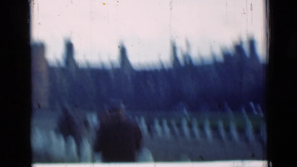 Soft, motion-blurred 8mm frame of visitors on the path, with the palace facade receding in the background.