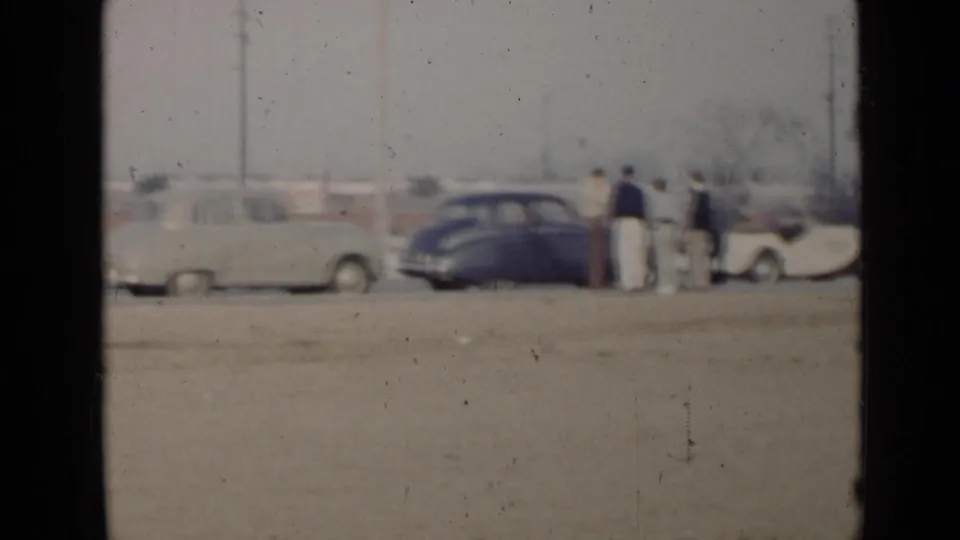In the San Diego rally footage, several men stand near a light sedan, dark coupe, and pale convertible on a dusty lot.