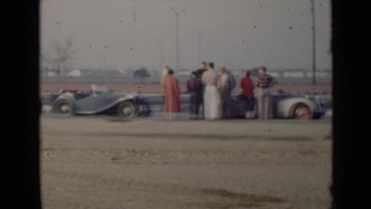 Group of adults stands beside several parked convertibles.