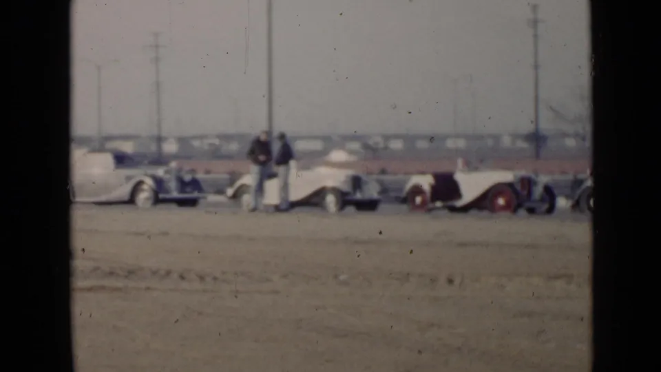 1949 San Diego home-movie frame showing a row of classic cars on a sandy lot with men standing near the vehicles.
