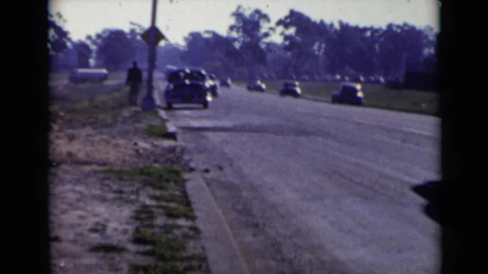 Roadside 8mm view in San Diego, 1949, with a dark car near the curb and additional cars farther along the street.