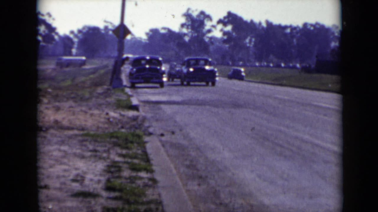 San Diego-area 1949 home-movie frame showing several classic cars driving toward the camera on a broad suburban road.