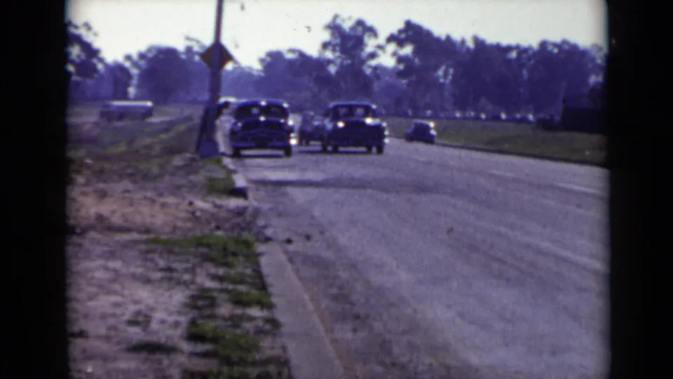 San Diego-area 1949 home-movie frame showing several classic cars driving toward the camera on a broad suburban road.