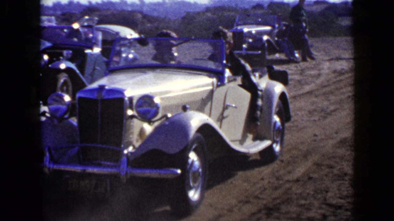 Cream classic convertible on a dirt road with other vintage cars nearby.