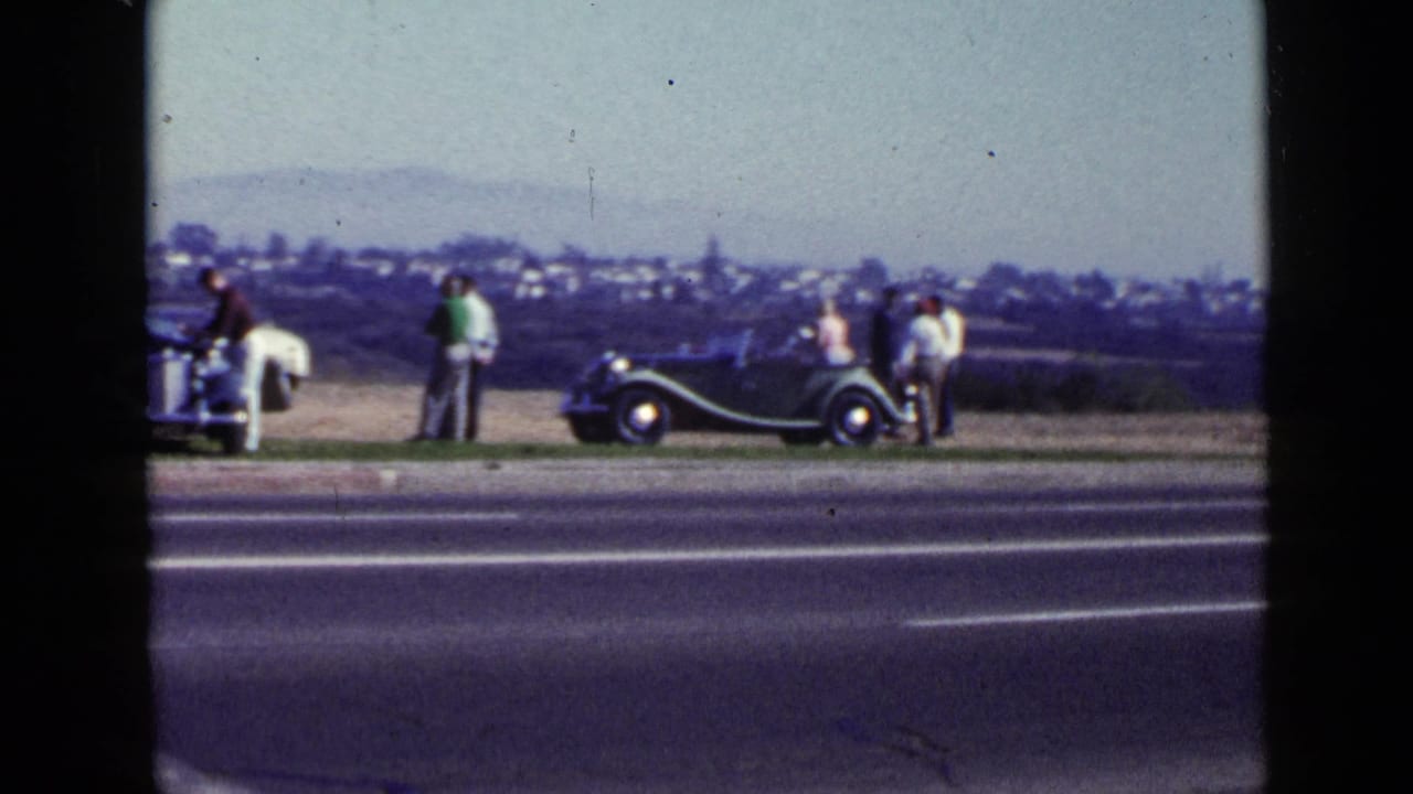 1949 San Diego roadside view with adults gathered near a dark convertible and a light-colored vintage car.