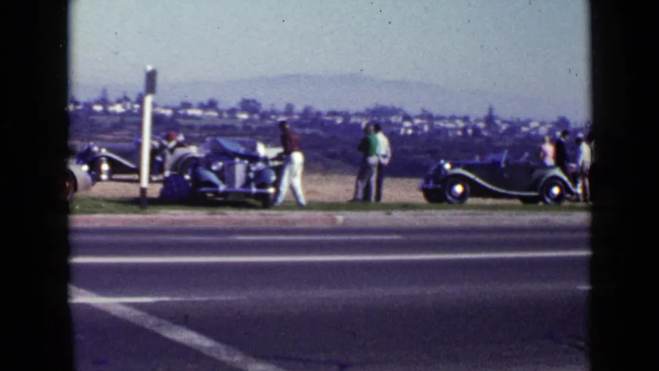 1949 San Diego roadside scene with adults, parked classic cars, a roadside post, and distant hills.