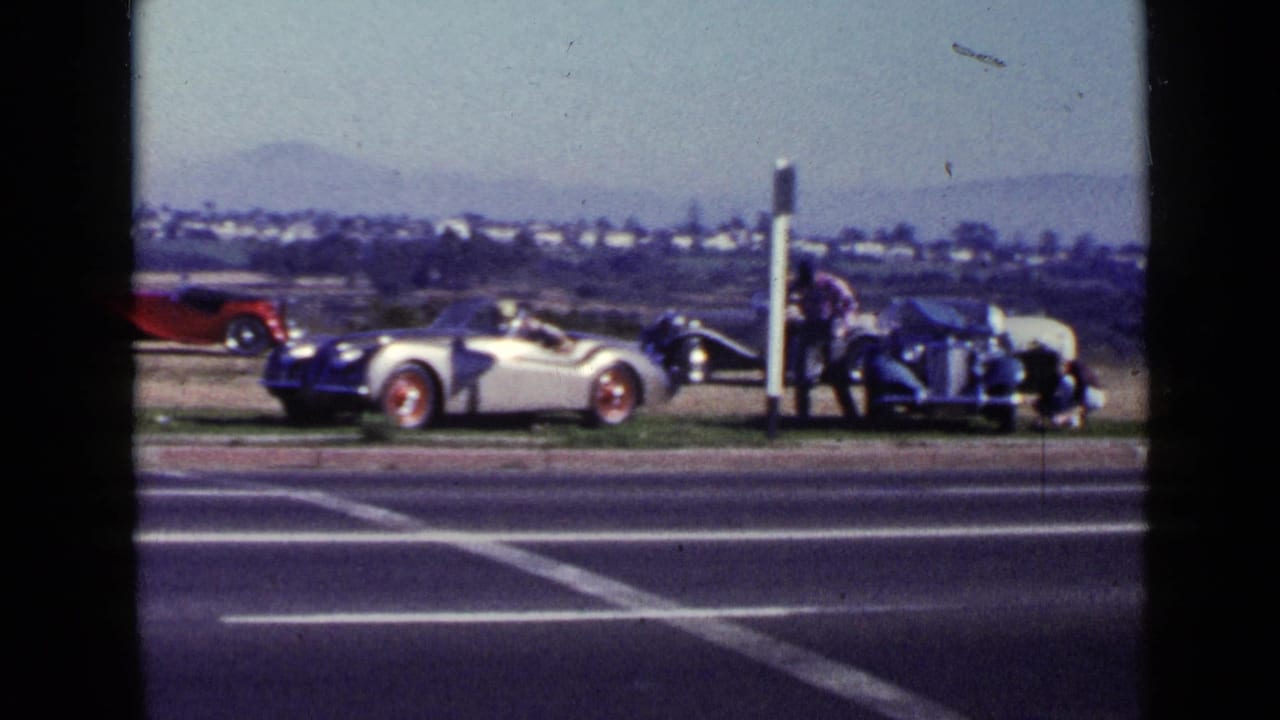 1949 San Diego roadside view with a silver convertible, red roadster, dark vintage car, and an adult walking near the vehicles.