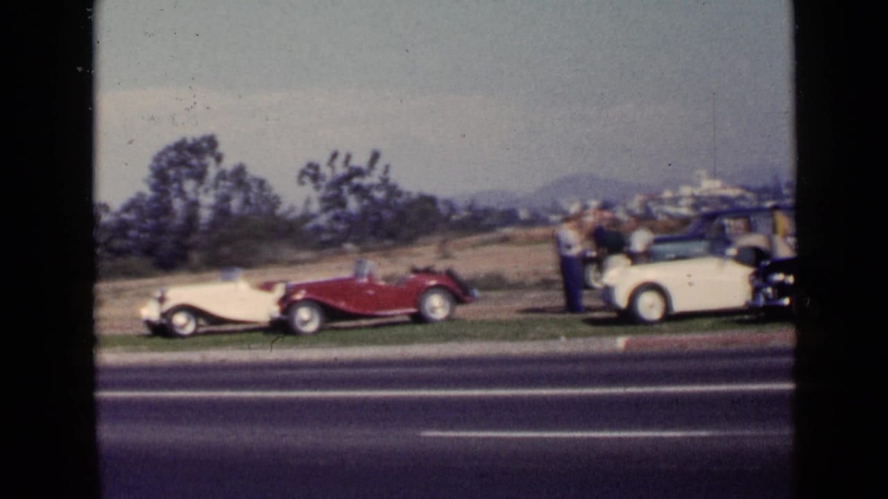 1949 San Diego frame with red and cream antique cars parked beside a highway as adults gather at the right edge.