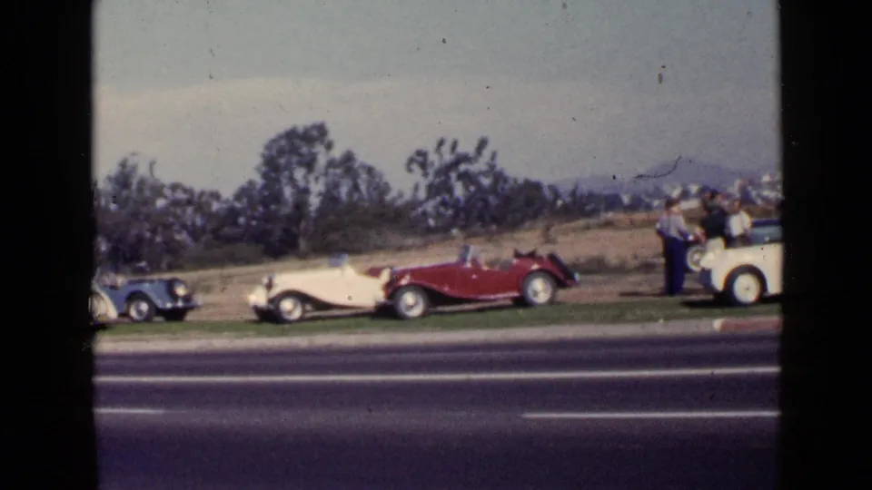 1949 San Diego home-movie frame showing blue, red, and cream antique cars displayed along a grassy roadside.