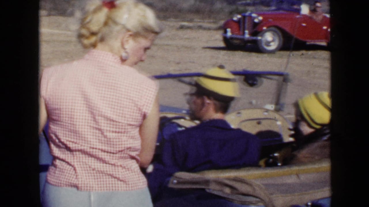 In 1949 San Diego footage, a woman stands near a blue convertible while a man in a yellow cap sits in the driver's seat.