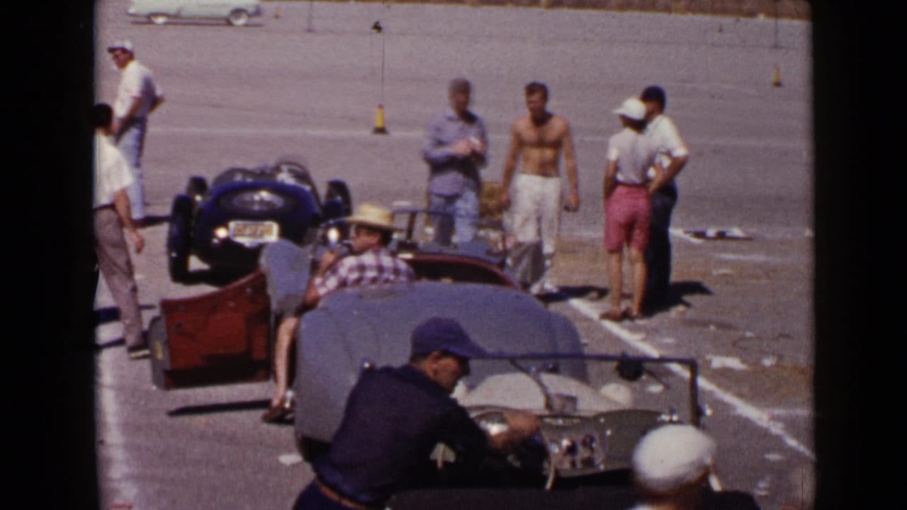 San Diego 1949 home-movie frame showing men gathered near open-top sports cars on a paved lot.
