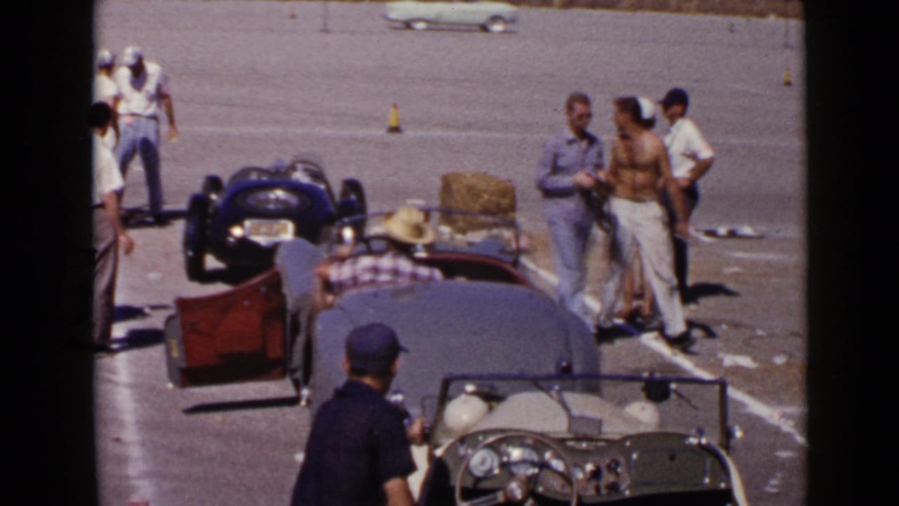 San Diego 1949 frame with men in casual clothing standing beside vintage sports cars on open pavement.