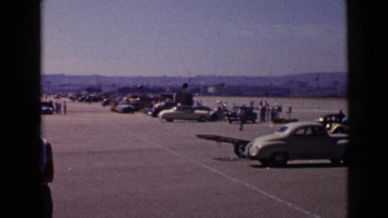 Rows of cars and spectators viewed through dark vertical framing.