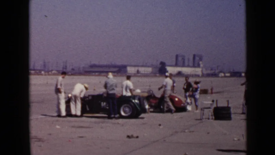Men in mid-century casual clothing inspect and stand beside vintage open cars in 1949 San Diego home-movie footage.