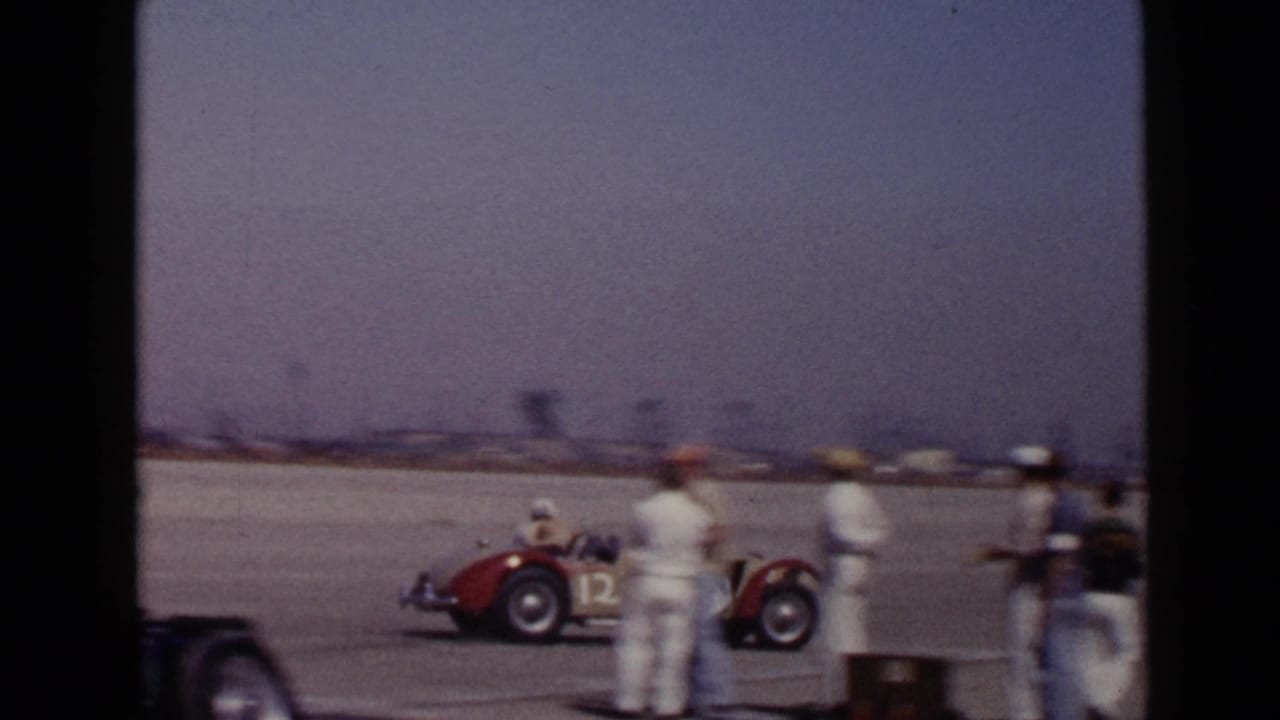 1949 San Diego racing footage showing a red open-wheel car passing crew members beside a paved track area.