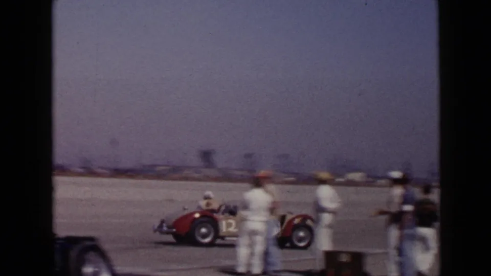 1949 San Diego racing footage showing a red open-wheel car passing crew members beside a paved track area.