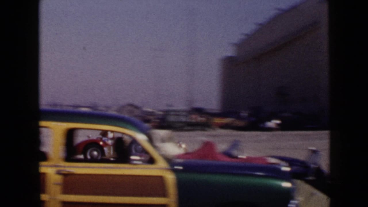 Colorful station wagon parked near race cars and people at a track area.