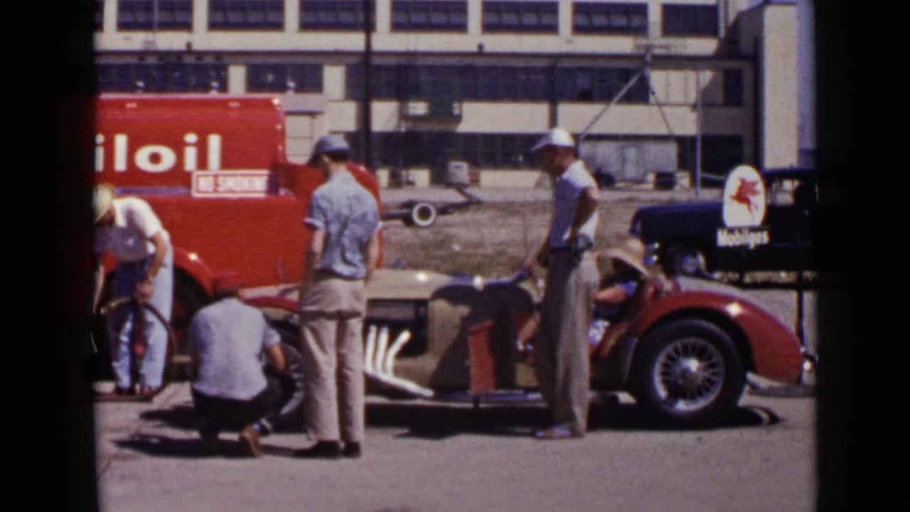 1949 San Diego home-movie frame showing men around a red convertible at a Mobil Oil service stop, with a truck and sign behind them.