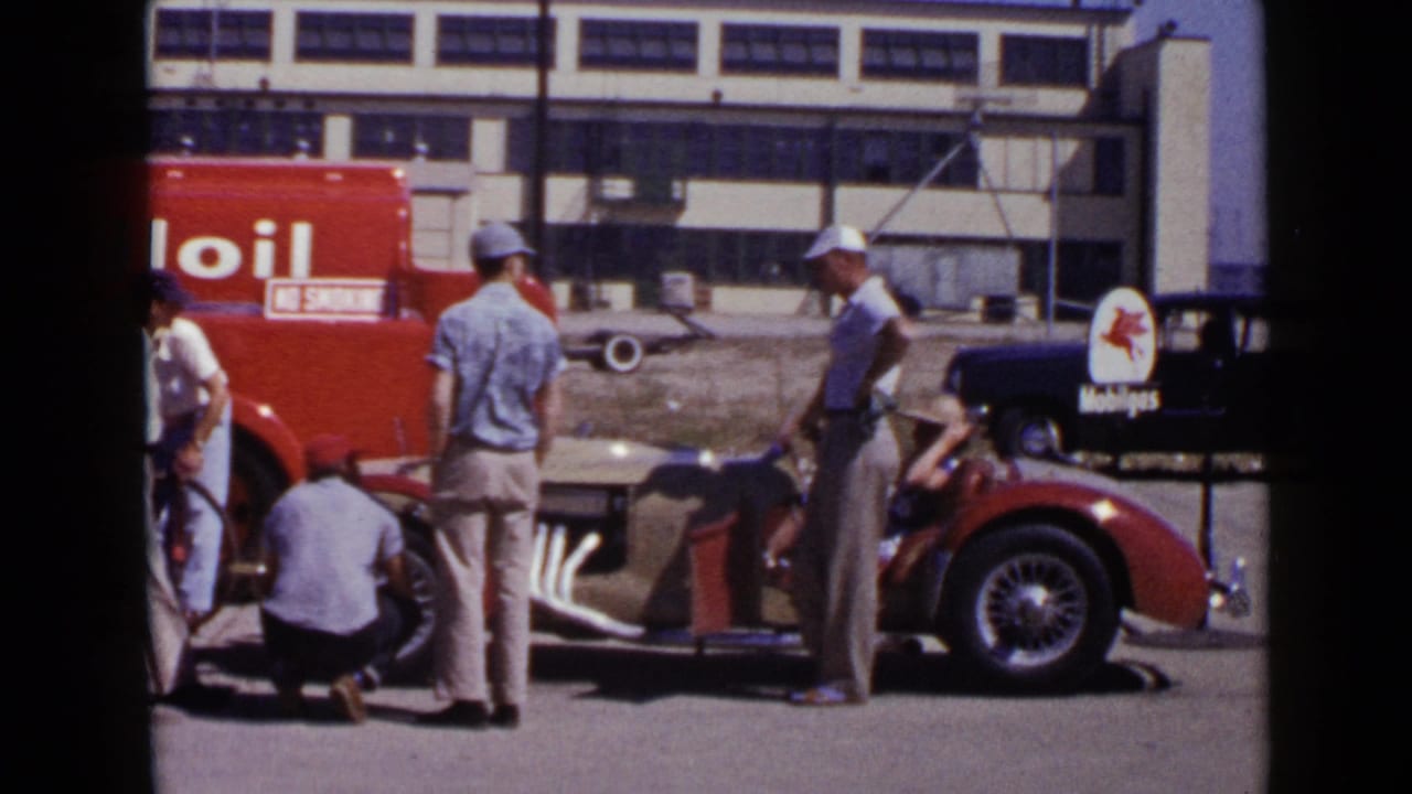 Men working near a red convertible with a Mobil Oil truck and Mobilgas sign in the background.