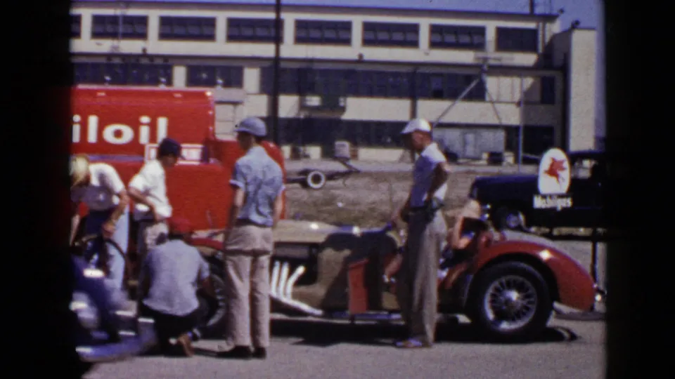 1949 San Diego home-movie frame showing men gathered at the side of a red convertible beside Mobil-branded service equipment.