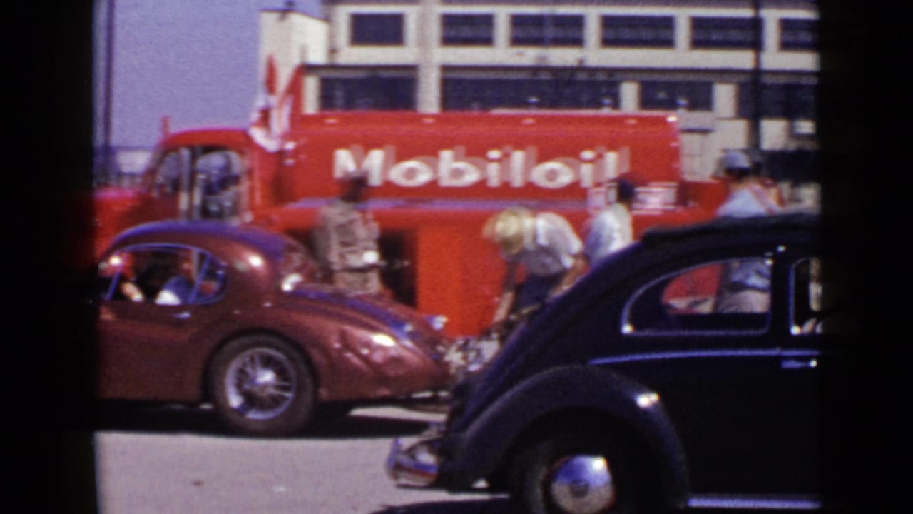 1949 San Diego home-movie frame showing a maroon racing car near a red Mobil oil truck, crew members, and a dark Volkswagen Beetle.