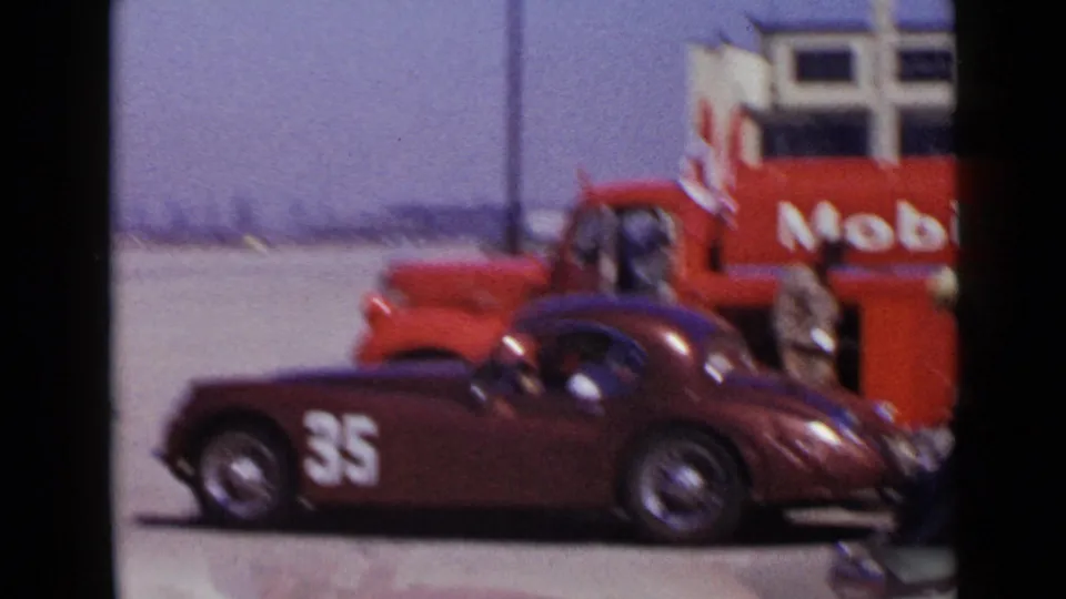 Soft 8mm frame from the 1949 San Diego clip showing the maroon number 35 race car near the red Mobil truck and crew.