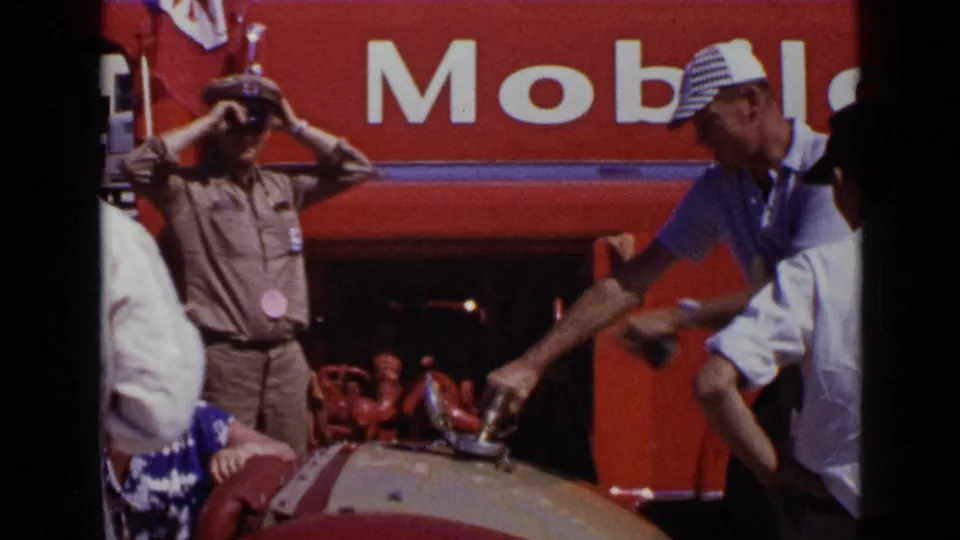 1949 San Diego home-movie frame showing a uniformed attendant adjusting his cap near a Mobil refueling area.